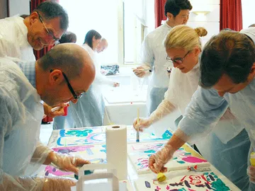 People paint happily on the table surface in a room.