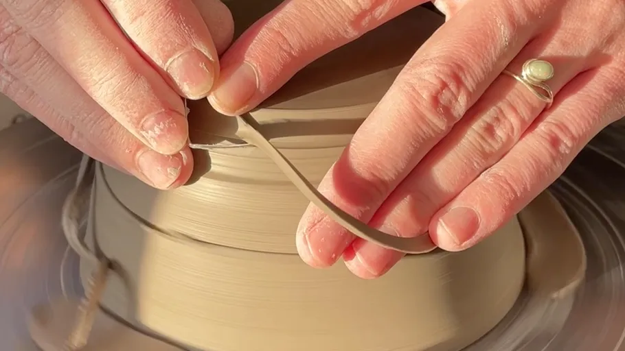 Hands shaping pottery on spinning wheel.