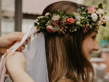 Blumenkranz wird auf Kopf angepasst; festliche Hochzeitsatmosphäre.