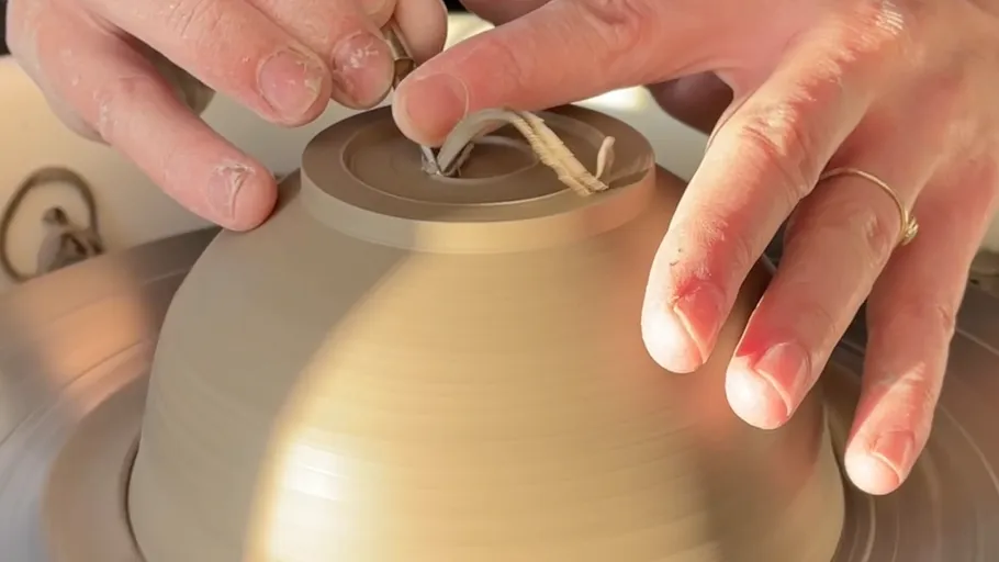 Hands shaping pottery on a potter's wheel.