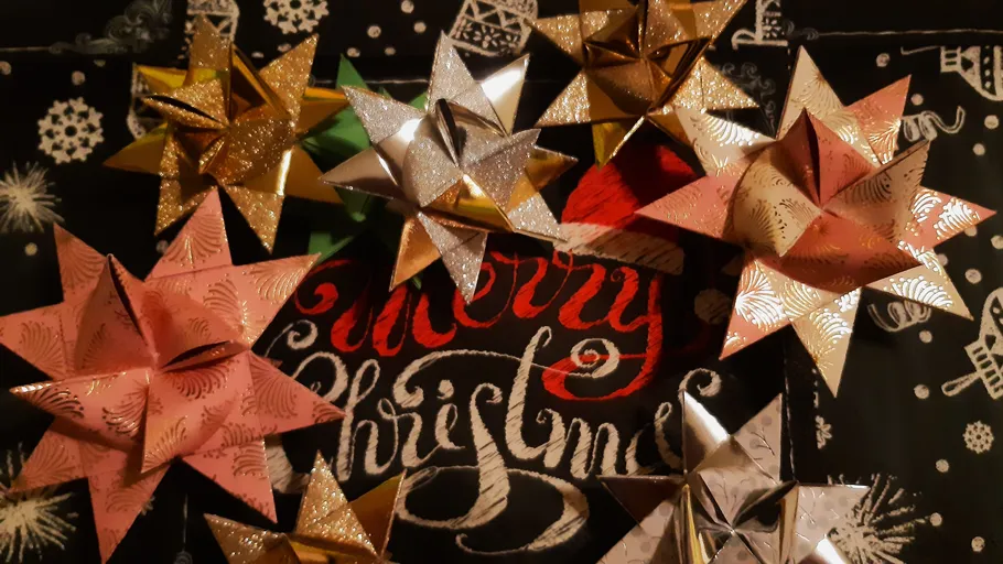 Bunte gefaltete Sterne auf 'Merry Christmas' Hintergrund.