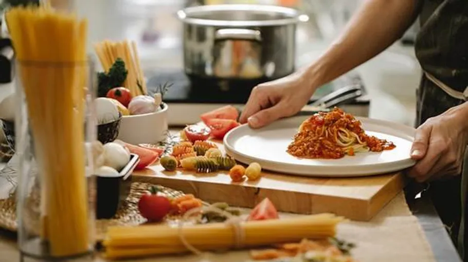 Person serviert Pasta in Küchenszene.