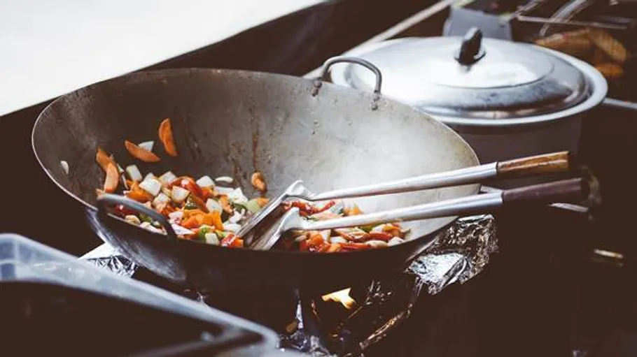 Wok cooking vegetables with two spatulas.