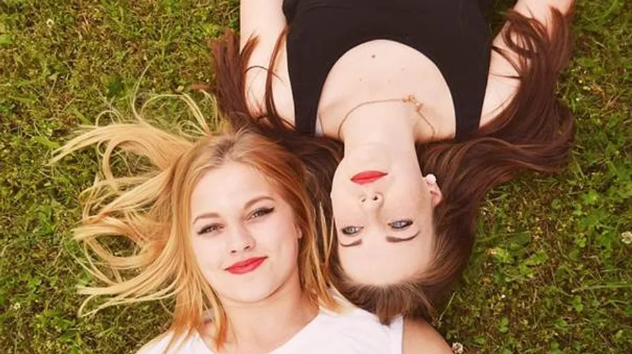 Two women lying on grass facing opposite directions.