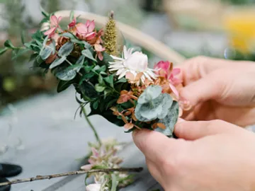 Blumenarrangement wird von Händen gehalten und geformt.