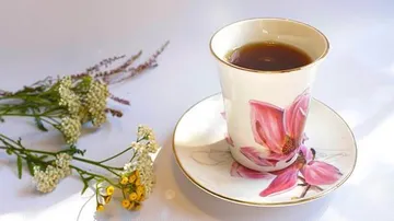 Tea in floral cup beside wildflowers.