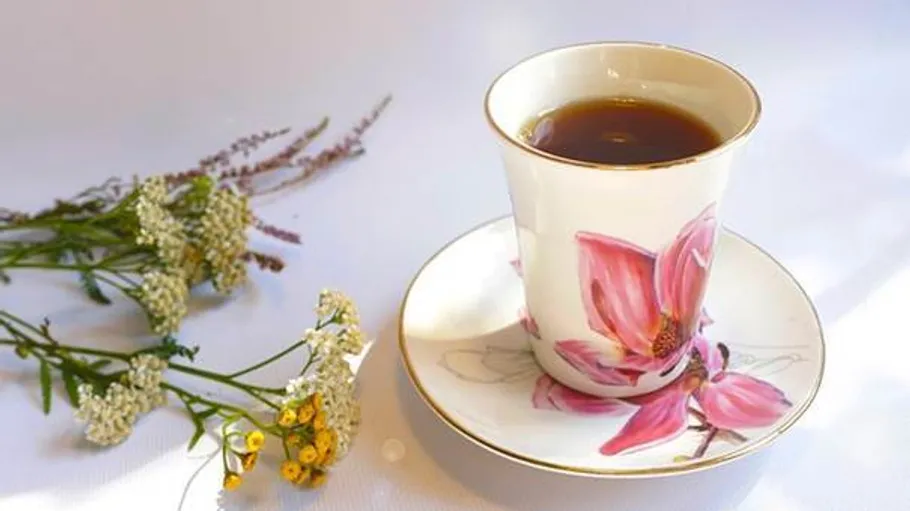 Tee in Blumetasse neben Wildblumen.