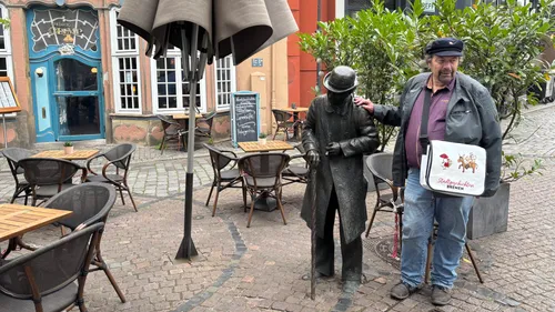 Man posing with statue outside a cafe.