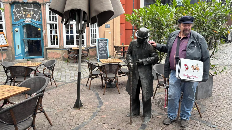 Mann posiert mit Statue vor einem Café.