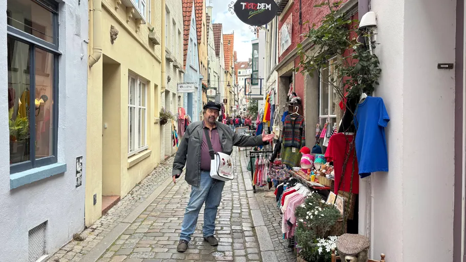 Mann gestikuliert auf Kopfsteinpflasterstraße bei Geschäften.