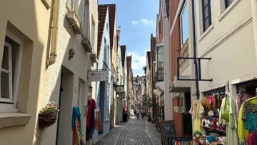 Narrow cobblestone street with colorful shops, daytime.
