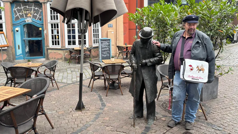 Mann steht neben Statue im Straßencafé.