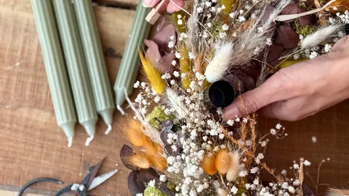 Hands arranging dried flowers centerpiece on table.