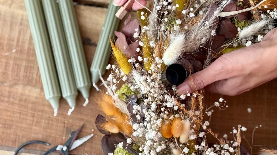Hände arrangieren Trockenblumen-Mittelstück auf Tisch.