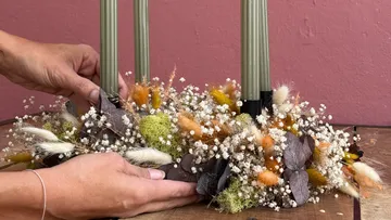 Hände arrangieren Trockenblumen um Kerzen.