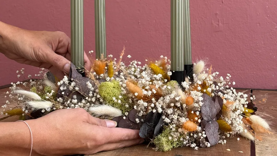 Hände arrangieren Trockenblumen um Kerzen.