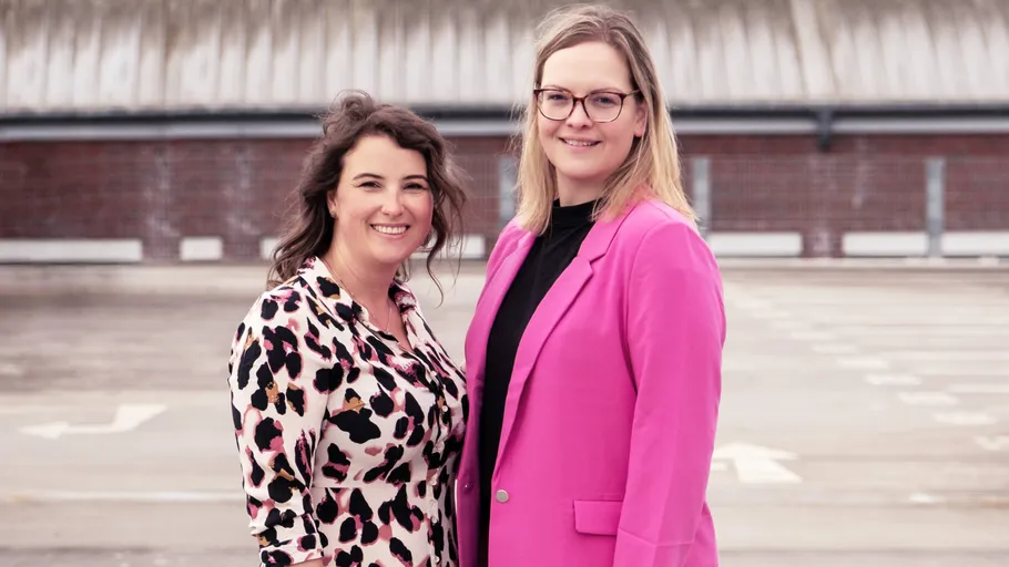 Two women standing on a rooftop parking area.