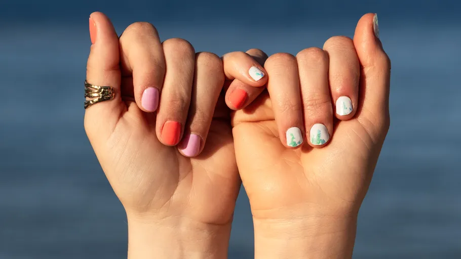 Hands with colorful nails by the sea.