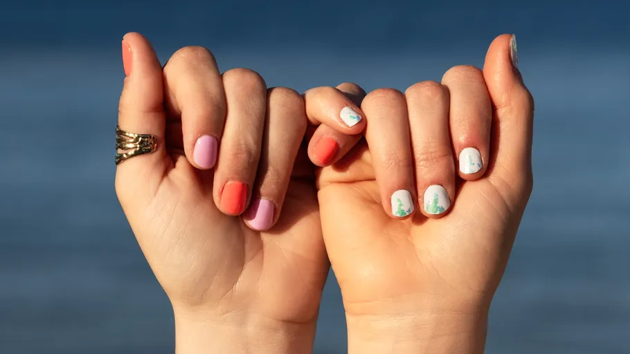 Hände mit buntem Nagellack am Wasser.