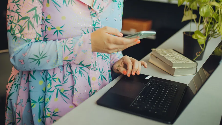 Person nutzt Handy neben offenem Laptop.