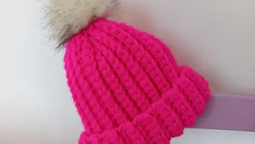 Pink gestrickte Mütze mit Fellbommel, weißer Hintergrund.