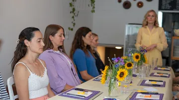 Frauen sitzen am Tisch, meditieren, dekorierter Tisch mit Bastelwerkzeug und Blumen.