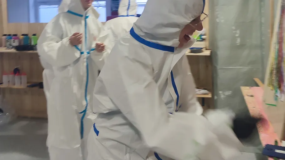 People in protective suits painting indoors.