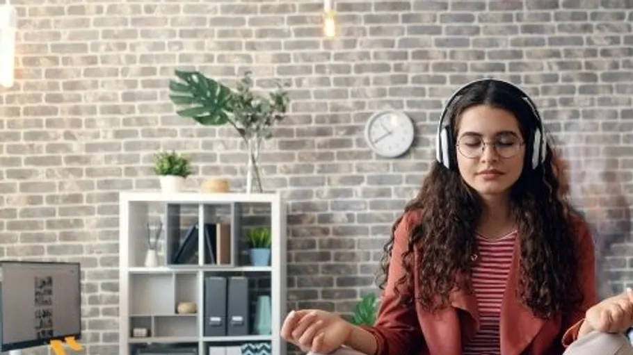 Woman meditating with headphones in modern office.