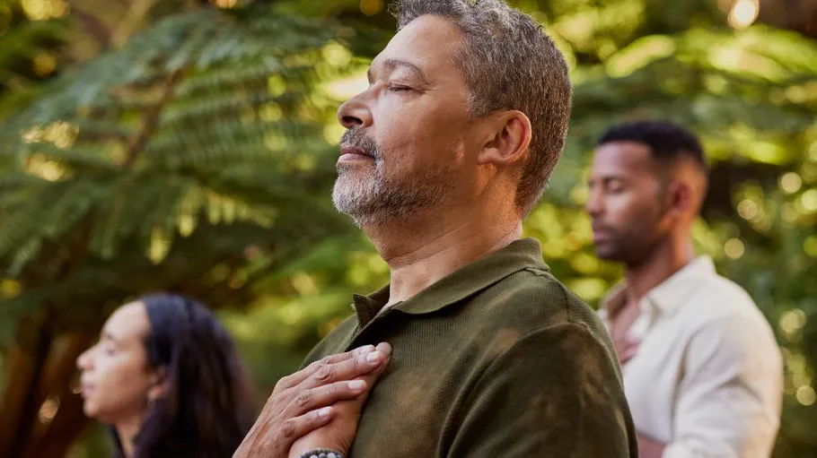 Three people meditating in lush forest.