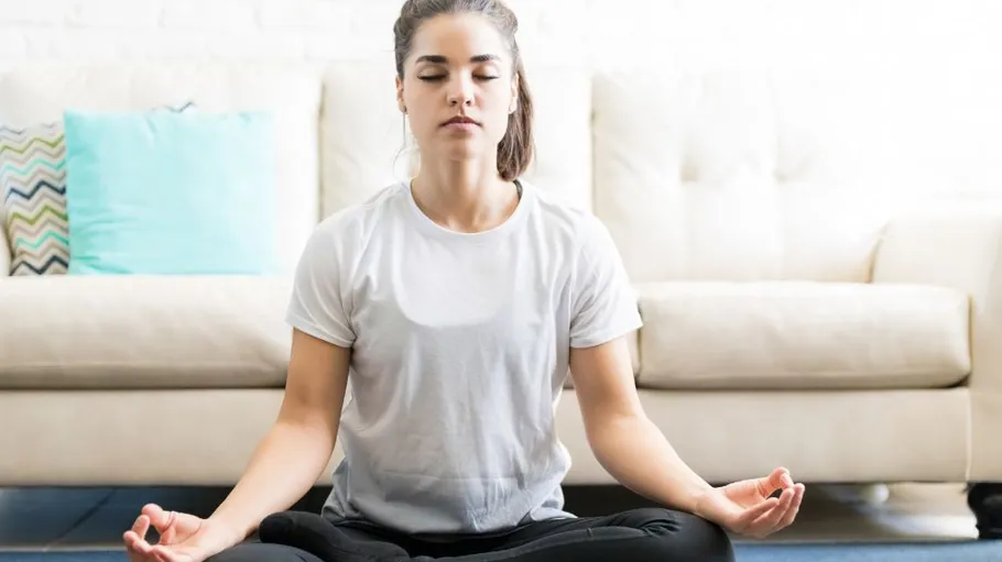 Woman meditating on floor in living room.