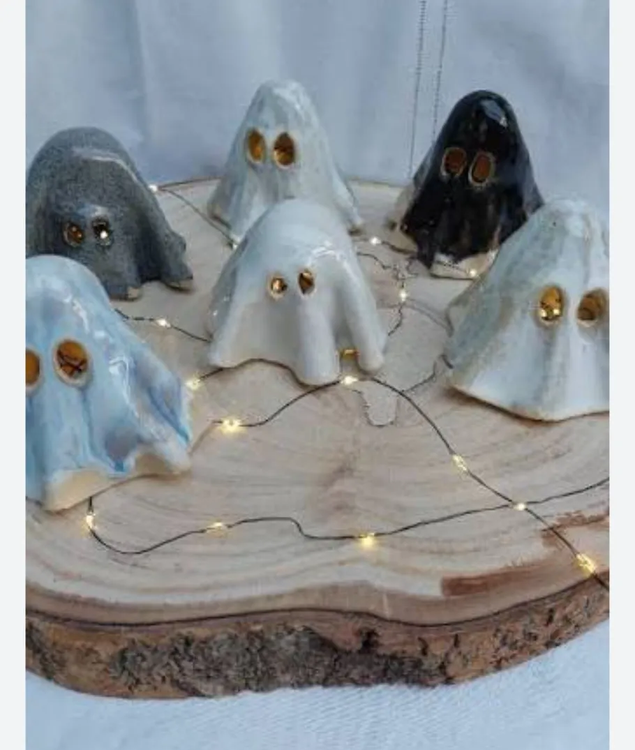 Ceramic ghosts on wooden slab with lights.