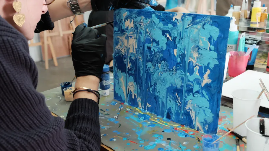 Artist painting blue abstract artwork on canvas.