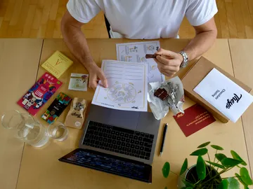 Person hält Schokolade und Arbeitsblätter am Tisch.