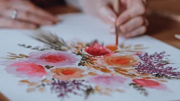 Person malt Blumen auf weißem Papier.