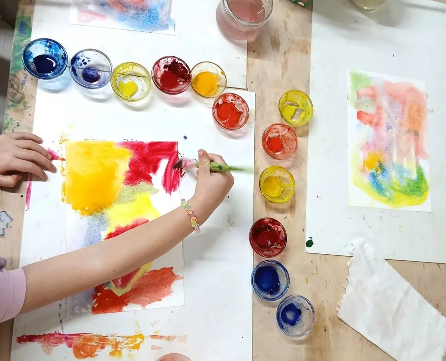 Child painting with brush on colorful canvas.