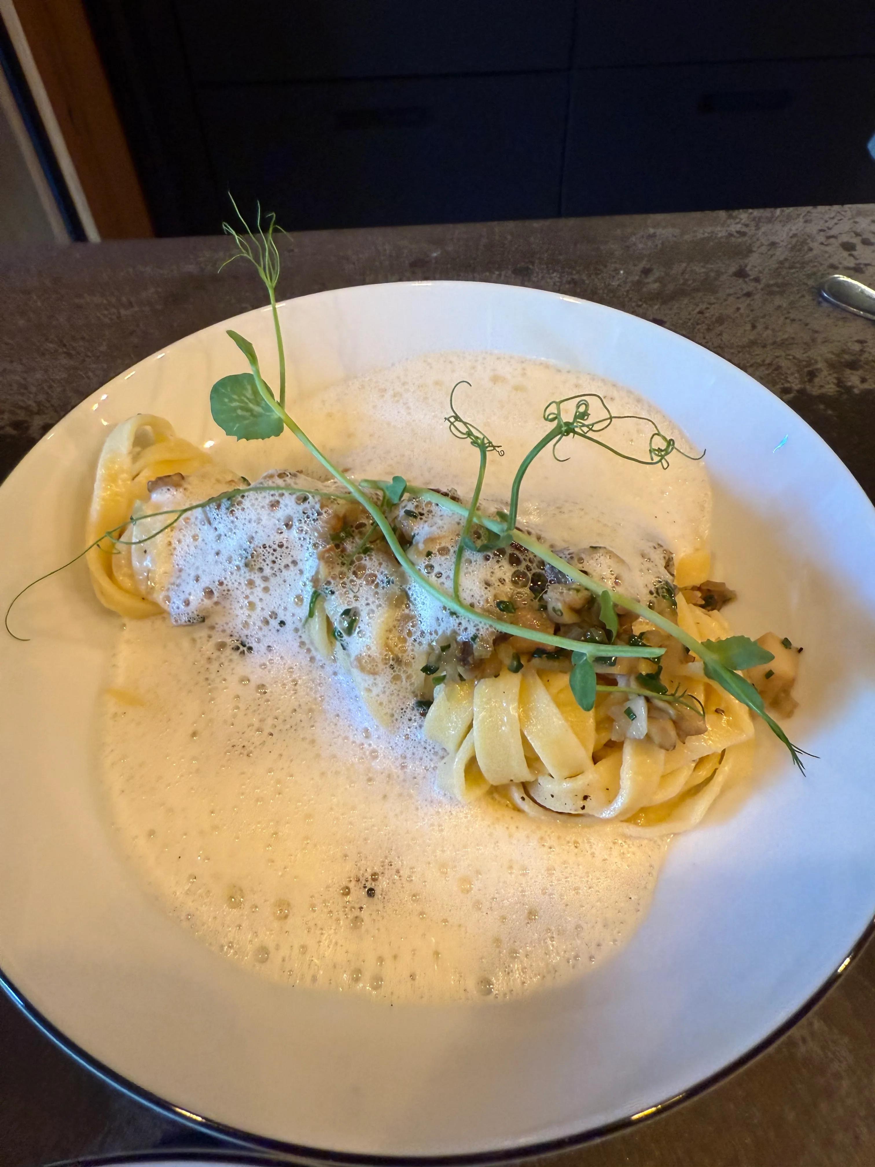 Pasta mit Schaum und Sprossen in weißer Schüssel.