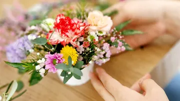 Hands arranging colorful flowers in vase.