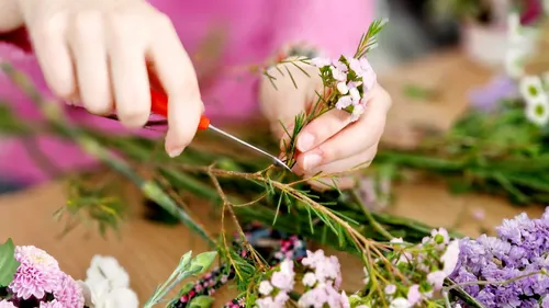 Person trimming flower stems on table.
