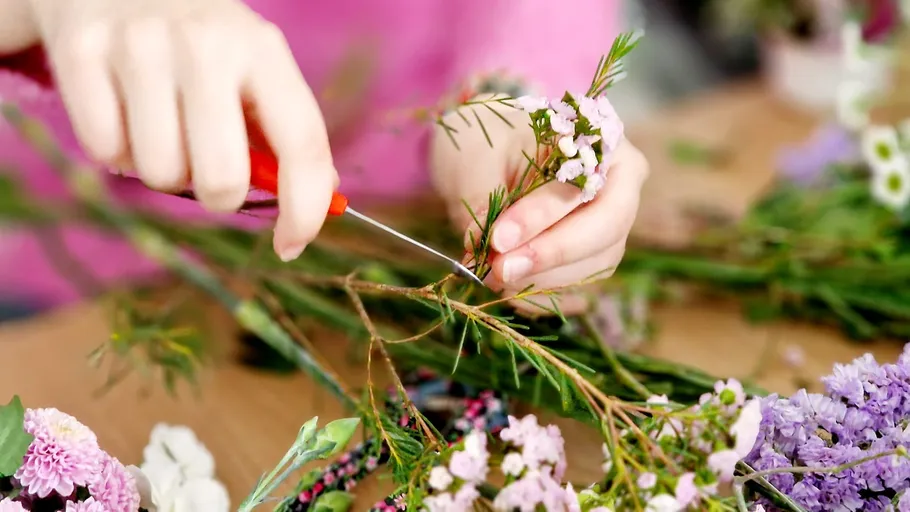 Person trimming flower stems on table.