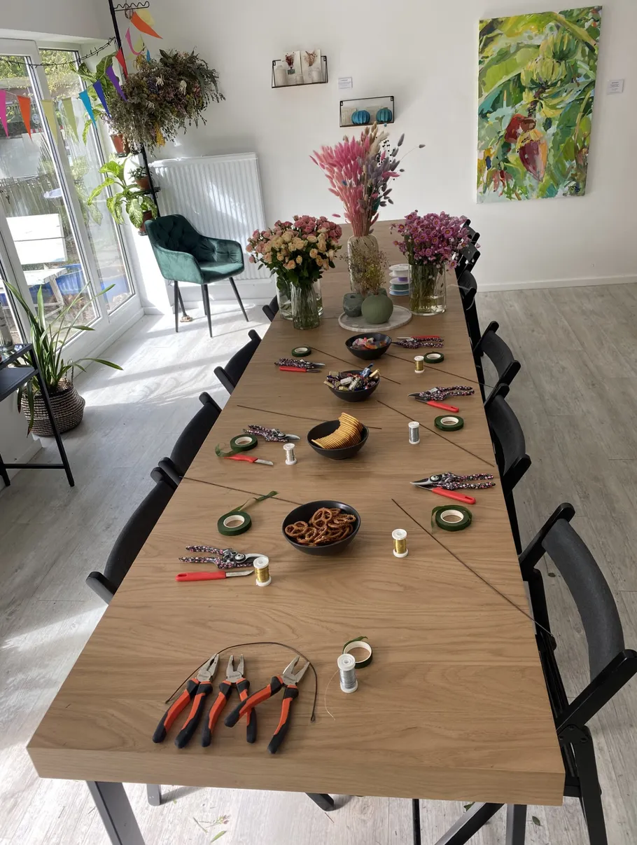 Tisch mit Blumen und Werkzeugen in hellem Raum.