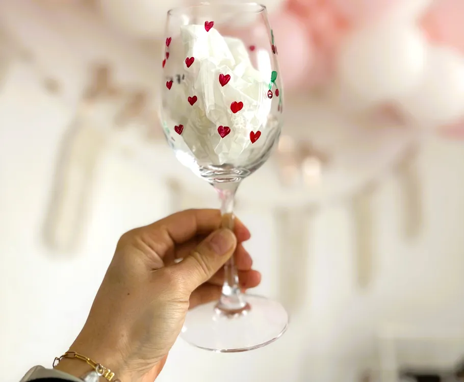 Hand hält dekoriertes Glas mit roten Herzen.