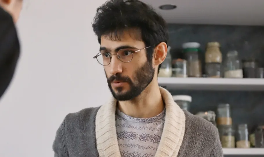 Mann mit Brille steht neben Regalen mit Gläsern.