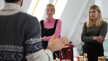 Two women listening to a person indoors.