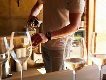 Ein Mann schenkt Wein in ein Glas am Tisch.