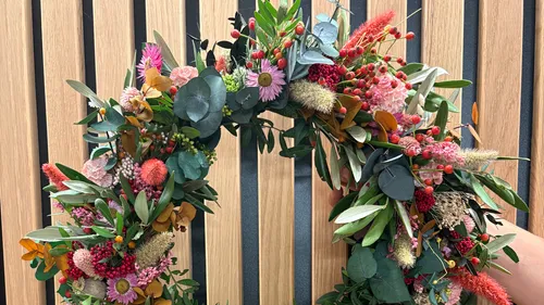 Bunter Blumenkranz vor Holzwand gehalten.