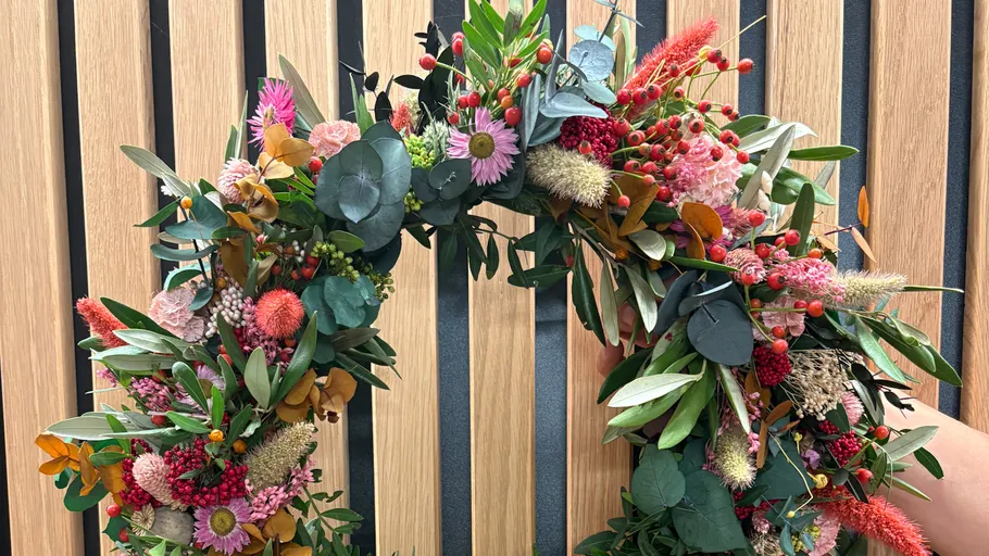 Bunter Blumenkranz vor Holzwand gehalten.