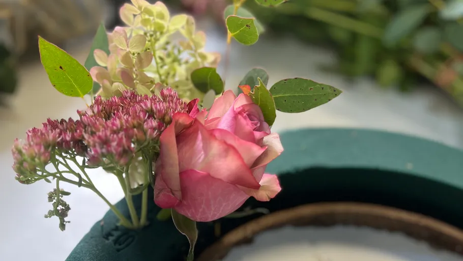Pink rose in floral arrangement on green base.
