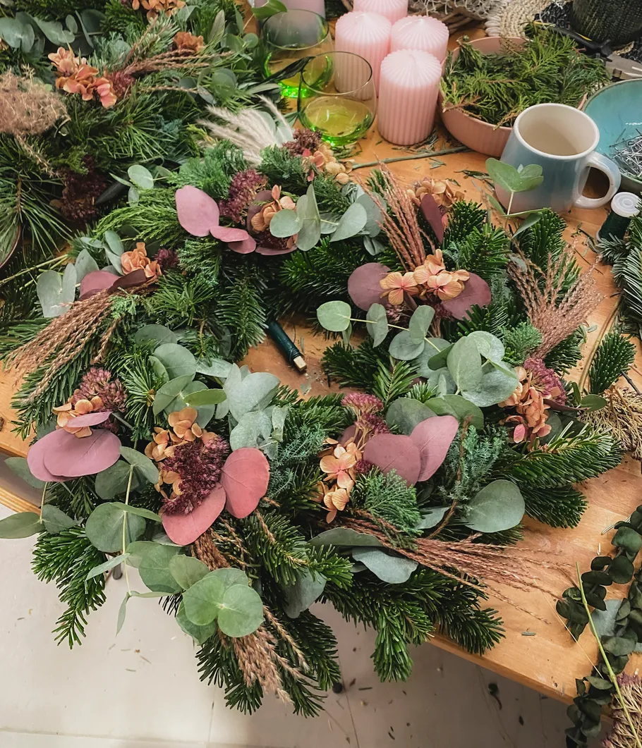 Dekokranz mit Grün und Blumen auf Tisch.