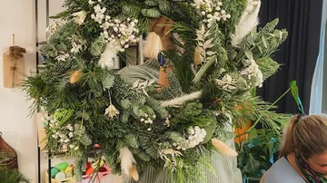 Person holding large decorated green wreath indoors.