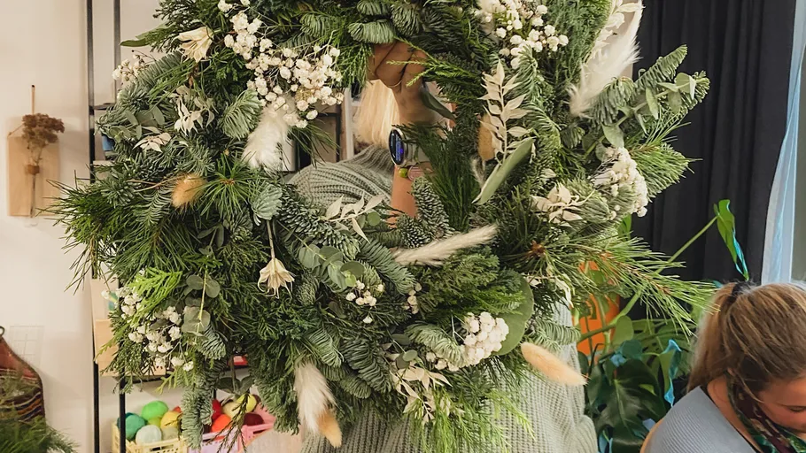 Person holding large decorated green wreath indoors.